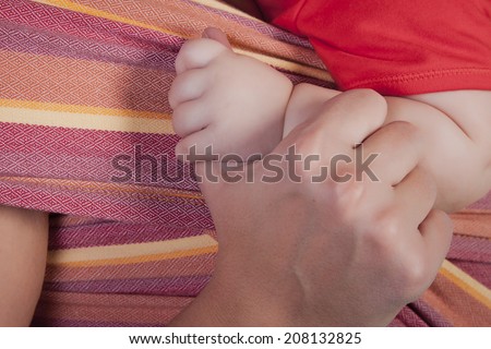 mother holding baby's hand on the background of the sling, closeup
