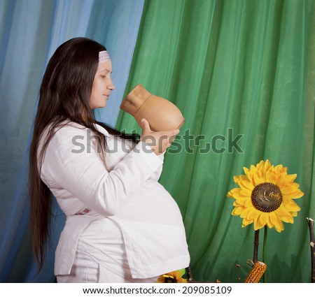 Pregnant woman in national dress drinks water from a jug, Slavic peoples, Russian and Ukrainian national style, rustic style