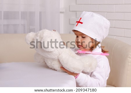 Little beautiful girl in costume of doctor treats a teddy bear