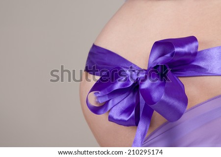 belly of a pregnant woman with a purple ribbon closeup concept in anticipation of surprise