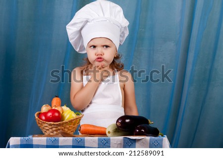Little cook prepares healthy food, cheery kitchen boy at the table, scullion makes pensive face