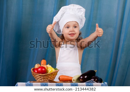 Little cook prepares healthy food, cheery kitchen boy at the table, happy kitchen boy holding a basket of vegetables, shows the 