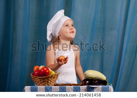 Little cook prepares healthy food, cheery kitchen boy at the table, happy kitchen boy holding a basket of vegetables. In the hands of onion, baby laughs from the smell of onions