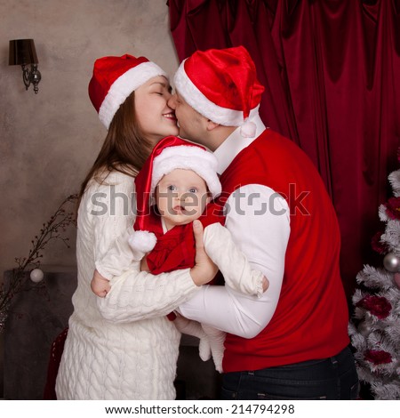 Dad, mom and baby in santa hat in anticipation of a happy Christmas. Family near Christmas tree,  the parents kiss