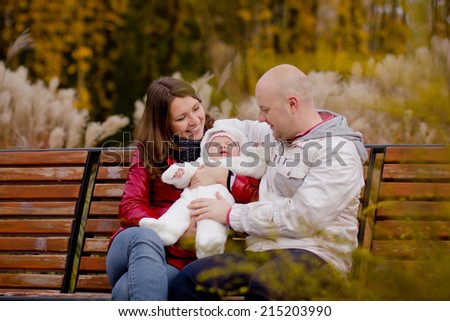 Happy family on a walk in the park. Dad, mom and baby are happy autumn weather and communication. Relax on a bench in the park