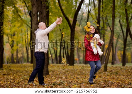 Happy family on autumn walk in the woods. Dad throws leaves up, mom and baby are happy autumn leaf fall