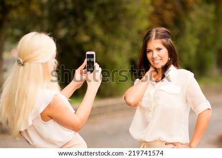 A woman takes pictures of another young woman on the phone, outdoors, recreation, entertainment