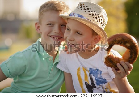 Two friends having fun talking in the park. One boy told a secret, the other is eating a muffin