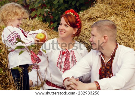 Ukrainian family in the village on a background of hay. Kid with apple