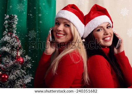 Two attractive young women friends near Christmas tree congratulate your friends and family by phone