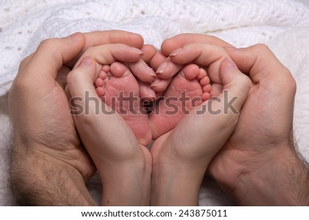 Legs newborn baby hands hug mom and dad, forming a heart. Symbolizes love, unity, caring, tender to the baby