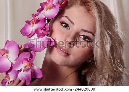 Closeup portrait of attractive blond female with gentle pink orchid flower in hair, skin care, perfect natural makeup, beauty salon