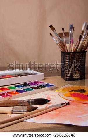 A set of brushes in a glass, paint, white sheet - a table of the artist, the creative process