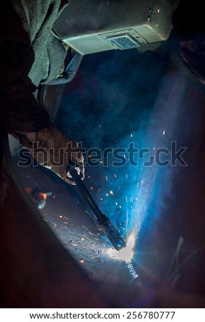 A tradesman welding steel on site at a engineering site at a mine. The sparks from the arc light the gloves and elding shield helmet.