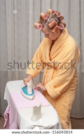 Girl with hair curlers in a dressing gown irons clothes.