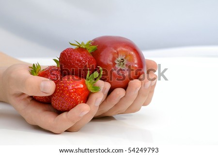Child holds in the hands apple and strawberries