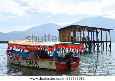 Lake Coatepeque, El Salvador - May 23, 2015: People are chilling on the pier by the lake and a tourist boat is seen on the foreground on May 23, 2015 at volcanic caldera Lake Coatepeque in El Salvador