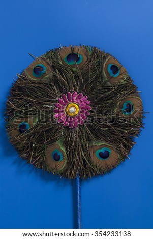 Round fan made of peacock feathers on blue background