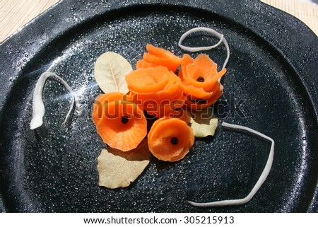 Decorative carrot salad in a black plate. Sun reflection on a black plate.