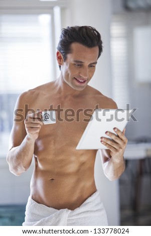 Young man wrapped in a towel with a cup of coffee and a tablet