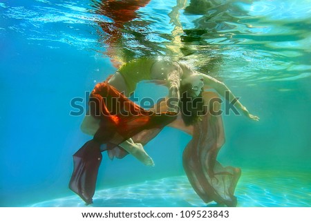 Beautiful girl under water with a long red fabric