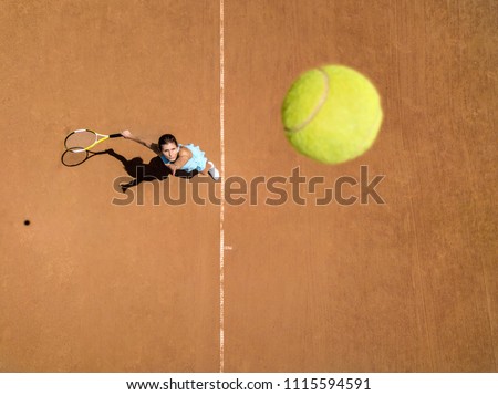 Pretty girl plays tennis on the court outdoors. She prepares to beat on a ball. Woman wears a light blue sportswear with white sneakers. Top view horizontal photo.