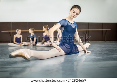 ballerina sitting on the floor in the splits and  dance class dancers practicing on the background