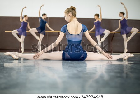 ballerina sitting on the floor with his back to the camera in the splits and dance class dancers practicing on the background