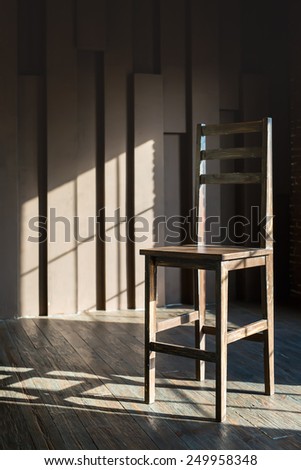 Large wooden brown chair stands on textural wooden parquet in the sun. The sun shines through the window.