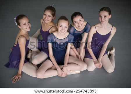 Five young ballerinas sitting on the floor and looking to the camera with smiles. Point shooting from above