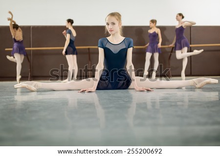 ballerina sitting on the floor front to the camera in the splits and dance class dancers practicing on the background