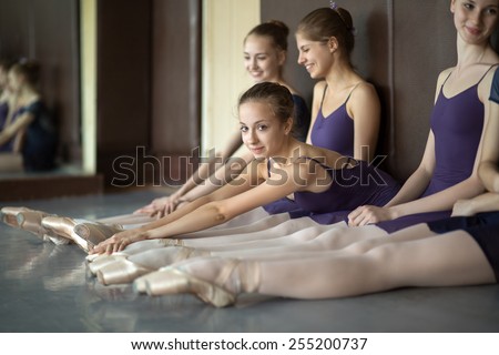 Five young dancers in the same dance costumes, resting sitting on the floor. Dance Class. Ballet School. Discussions yet with each other. One model looks to the camera.