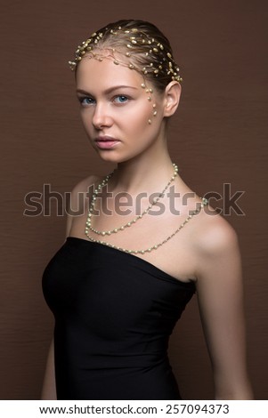 Portrait of a beautiful fashion model with jewelry on the neckline and hairstyle on brown background in studio