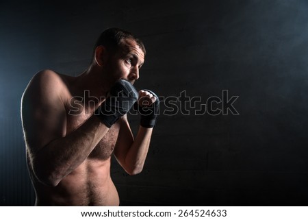 young boxer in light weight with bare-chested in fighting stance against a dark background in the studio