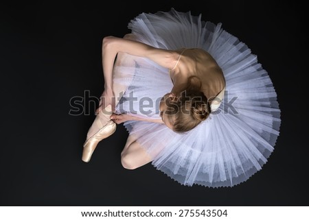 Young ballet dancer tying pointe sitting on the floor. Black studio background.