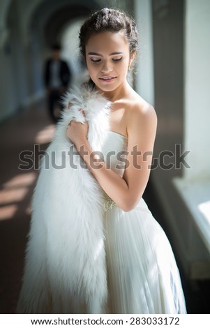Delicate bride with curly hair standing near the window