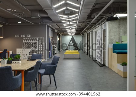 Coworking in a loft style. On the left there are tables with orange legs and blue chairs. On the table there are plants in the pots, pen holders, brick and a folder. Further to the left there is a
