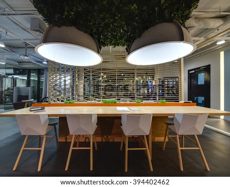 Interior in a loft style. Wooden table with stand for office supplies. There are grass decorations on the stand. Above the table hang large lamps with artificial leaves. There are notebooks on the