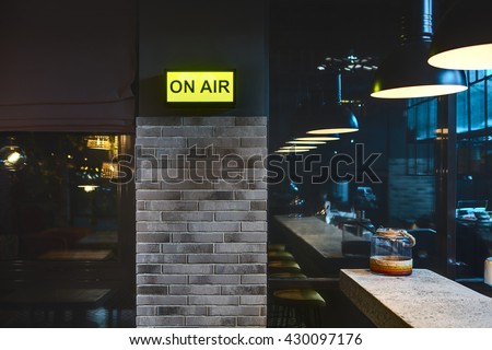 Half-lighted room in a mexican restaurant. There is a brick wall with glowing signboard and windows. On the right there is a light rack with jar on it and glowing lamps over it. Other side of the room