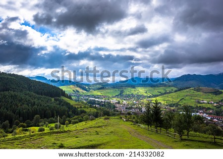 Storm clouds above a road on mountain village. Green grass and trees, grey clouds