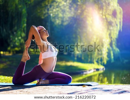 Young woman doing yoga in morning park near lake