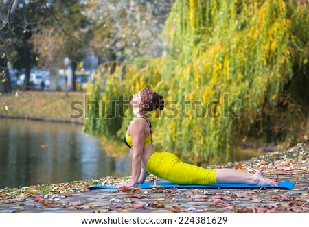 Young woman in yellow clothing doing yoga in the autumn Park near lake