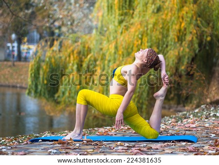 Young woman in yellow clothing doing yoga in the autumn Park near lake
