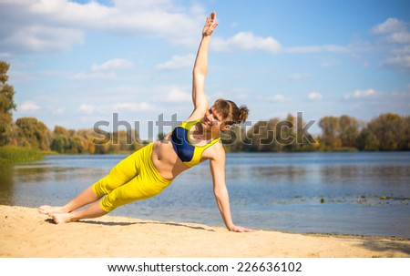 Young woman in yellow clothing doing yoga on the river bank