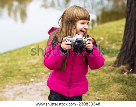 Happy baby girl laughing and playing with camera in autumn park near lake