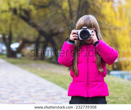 Happy baby girl playing with camera in autumn park near lake