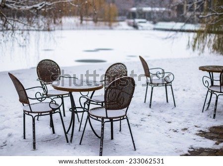 Round tables and wicker chairs with first snow in city cafe