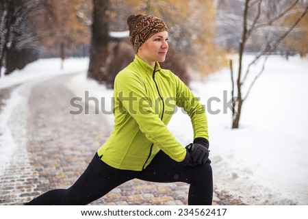 Young sport woman model doing exercises during winter training outside in cold snow weather in park