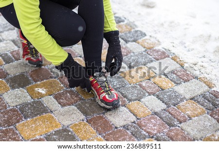 Young sport woman model tying running shoes during winter training outside in cold snow weather in park