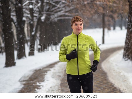 Young sport woman model  jogging during winter training outside in cold snow weather in park